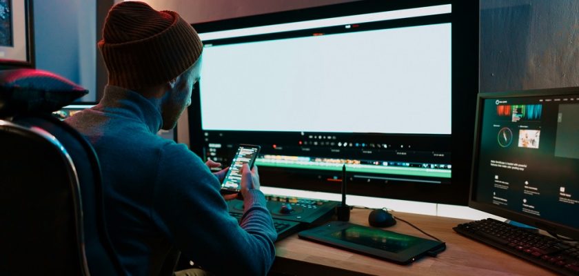 Male Video Editor sitting at his Computer using phone blank screen