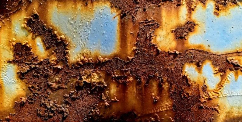 Corrosion - a rusted metal surface with blue and yellow paint